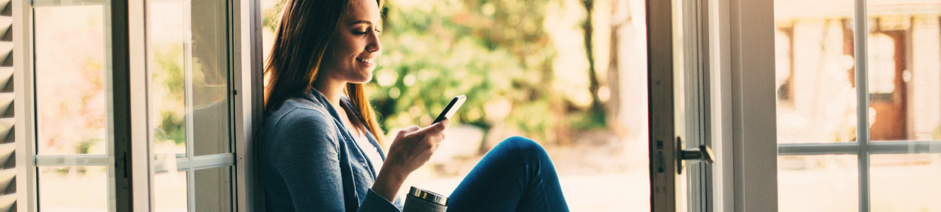 Woman sitting in a doorway looking and smiling at her phone