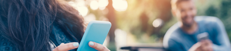 A woman holds her cellphone as she sits on a bench outside on a sunny day. 